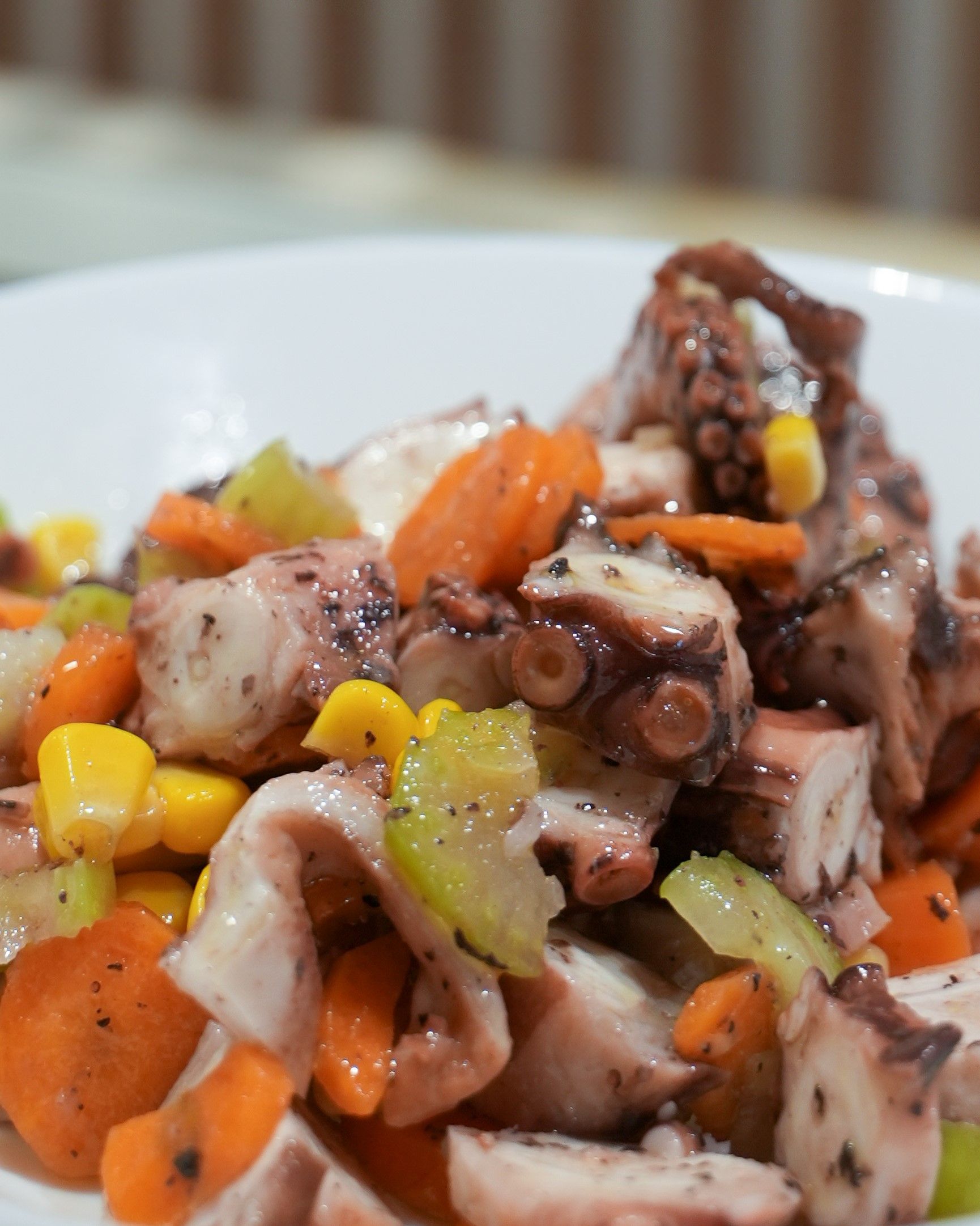 Insalata di polpo a cubetti con carote, sedano e mais su un piatto bianco.