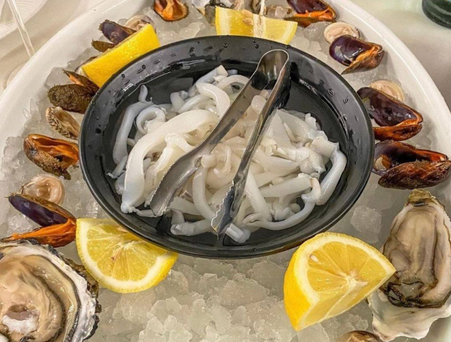 Piatto di frutti di mare con anelli di calamari crudi, cozze, ostriche e spicchi di limone su ghiaccio.