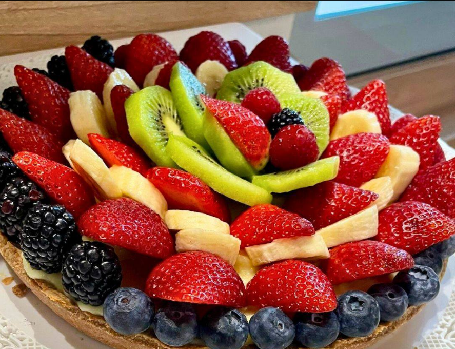 Torta di frutta colorata guarnita con fragole, kiwi, mirtilli, more e fette di pesca su un piatto
