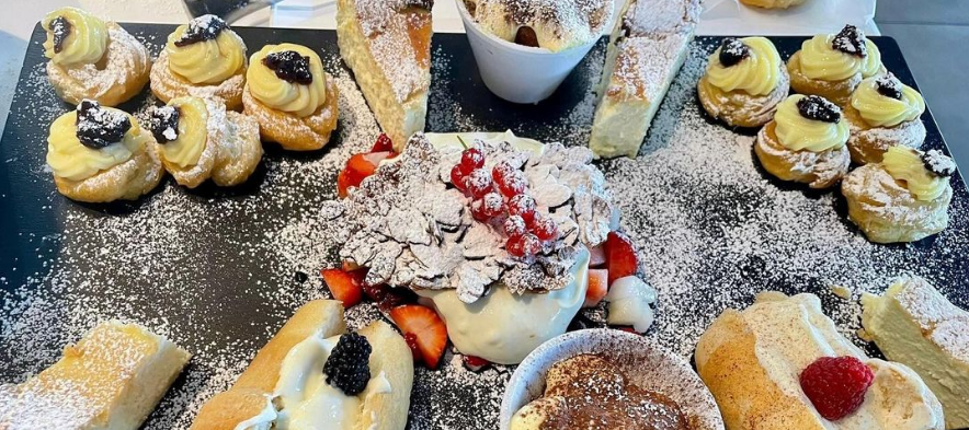 Un assortimento di pasticcini e girelle ripiene di crema, spolverate di zucchero a velo, su un vassoio da dessert.