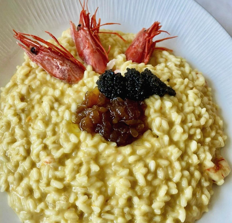 Piatto di cremoso risotto ai frutti di mare guarnito con tre gamberi, caviale e una cucchiaiata di salsa.
