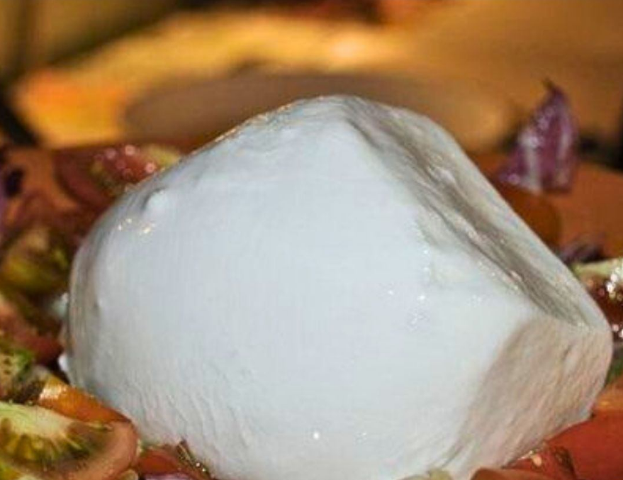 Una palla di mozzarella bianca su un piatto con guarnizioni colorate intorno.