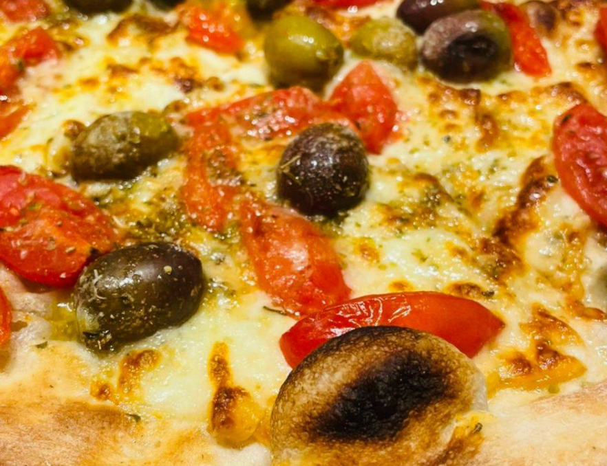 Primo piano di una pizza al formaggio condita con olive nere e fette di pomodoro rosso.