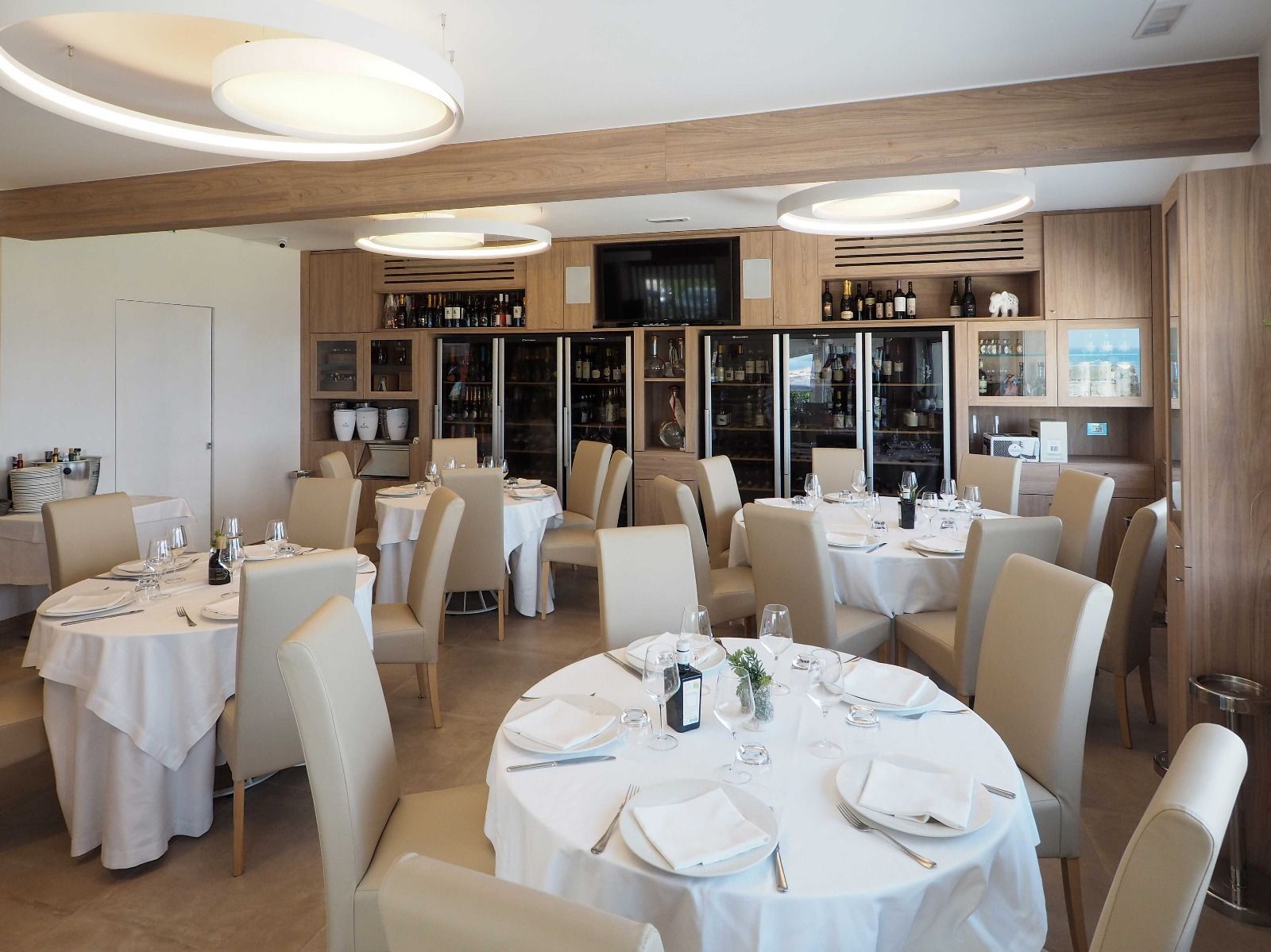 Elegante sala da pranzo di un ristorante con tovaglie bianche, tavoli apparecchiati e caldi dettagli in legno.