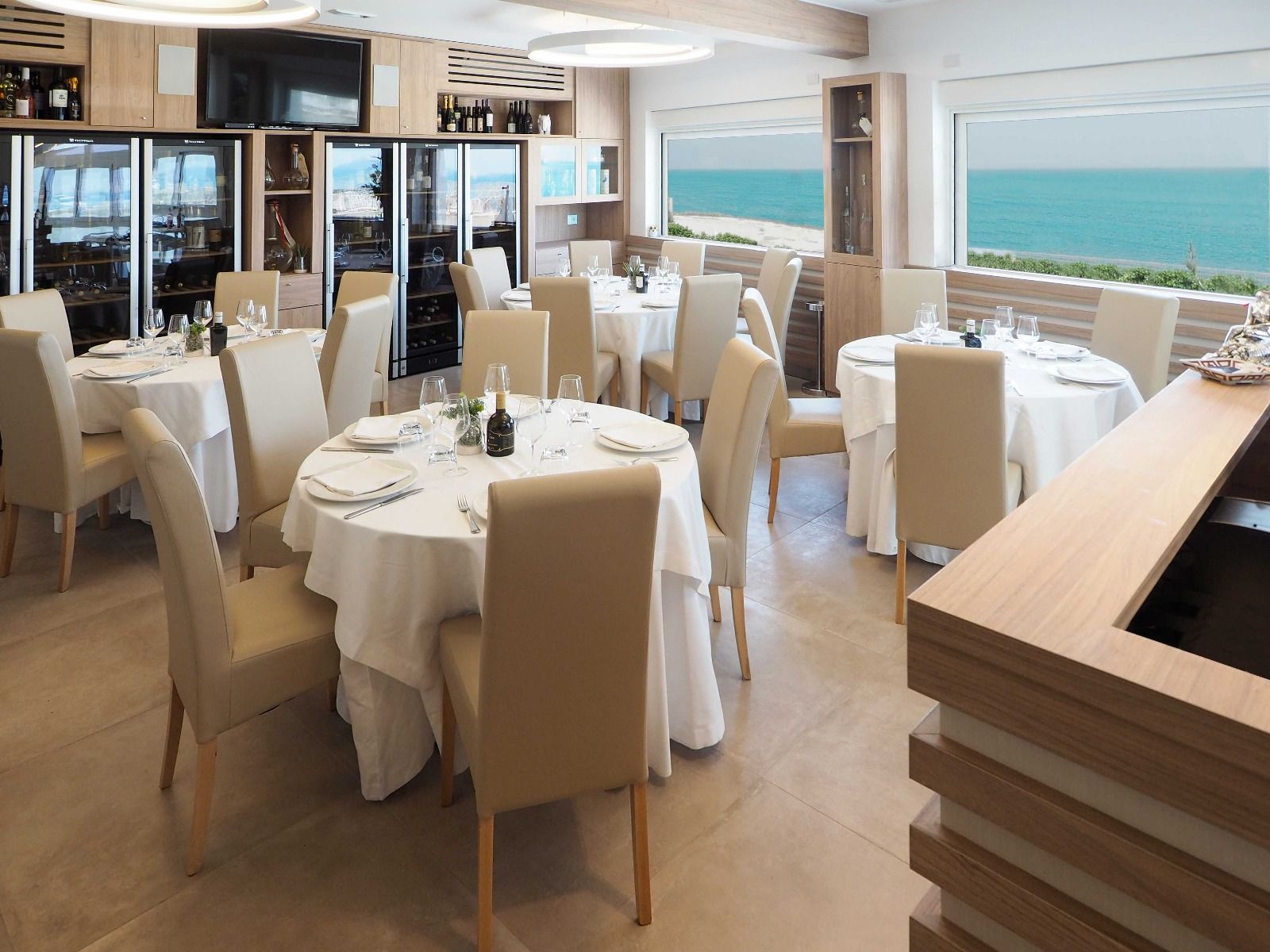 Elegante ristorante sul mare con tavoli apparecchiati con tovaglie bianche e vista sull'oceano attraverso ampie vetrate.