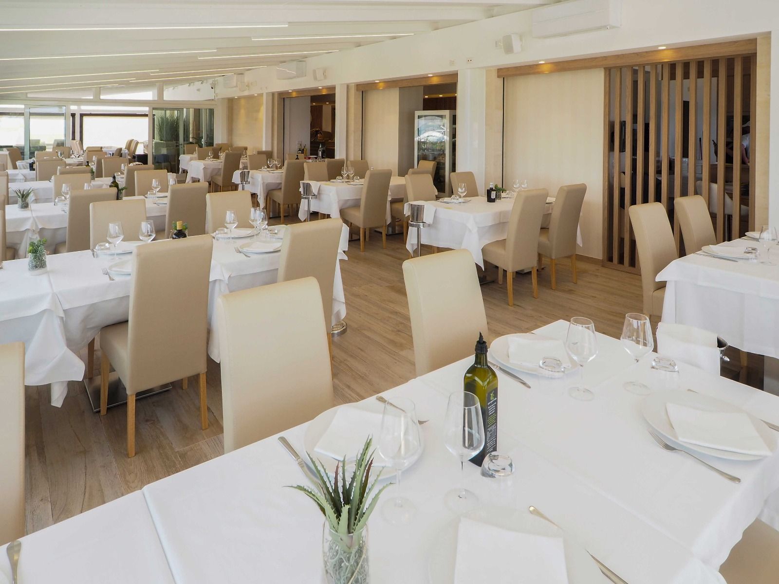 Sala da pranzo luminosa con tovaglie bianche, sedie beige e tavoli apparecchiati con cura.
