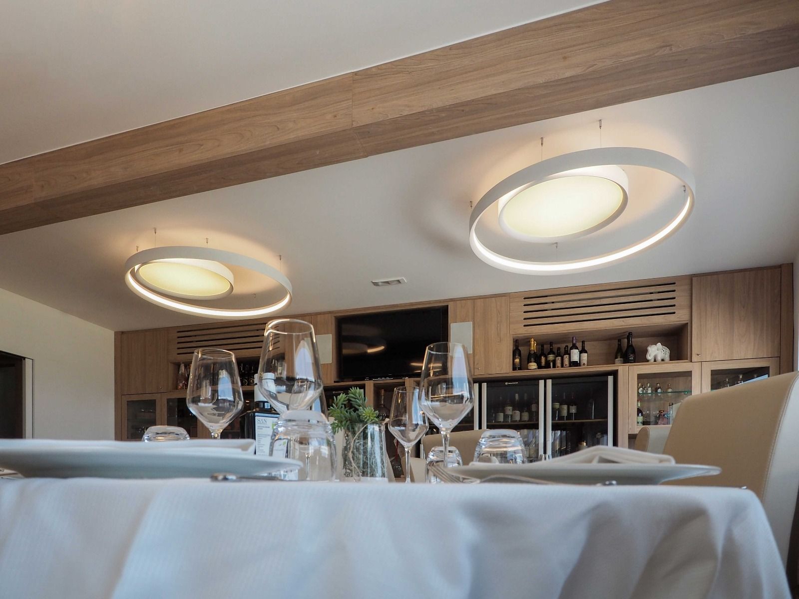 Elegante sala da pranzo con tavolo apparecchiato, calici da vino e moderne lampade a soffitto.