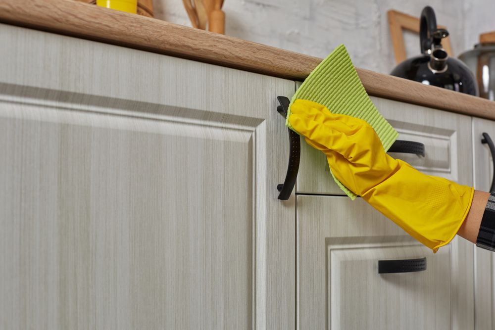 A person wearing yellow gloves is cleaning a kitchen cabinet with a cloth. — Happy Housekeepers in Kootingal, NSW