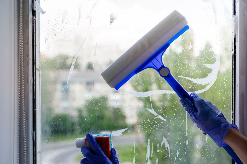 Person is Cleaning a Window With a Squeegee — Happy Housekeepers in South Tamworth, NSW