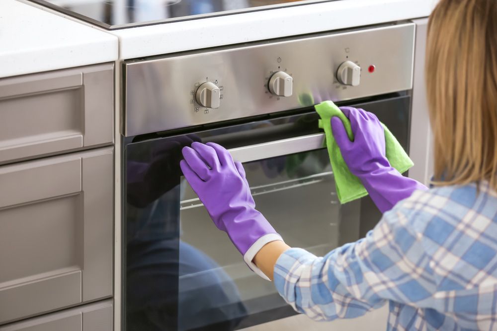 Woman Wearing Purple Gloves is Cleaning an Oven With a Cloth  — Happy Housekeepers in Manilla, NSW