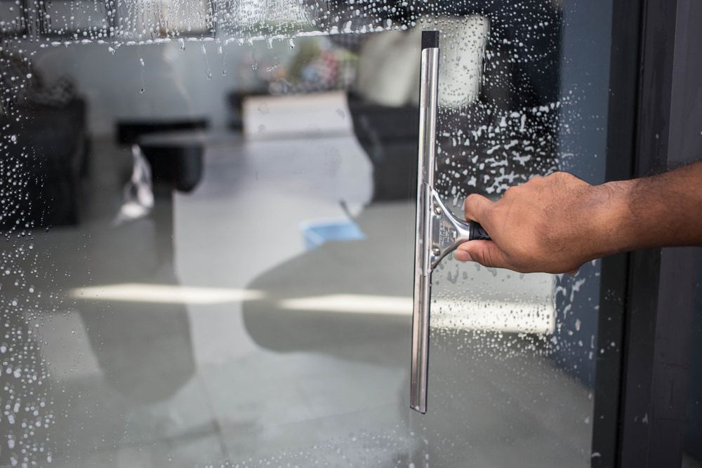 Person is Cleaning a Glass Door With a Squeegee — Happy Housekeepers in Manilla, NSW