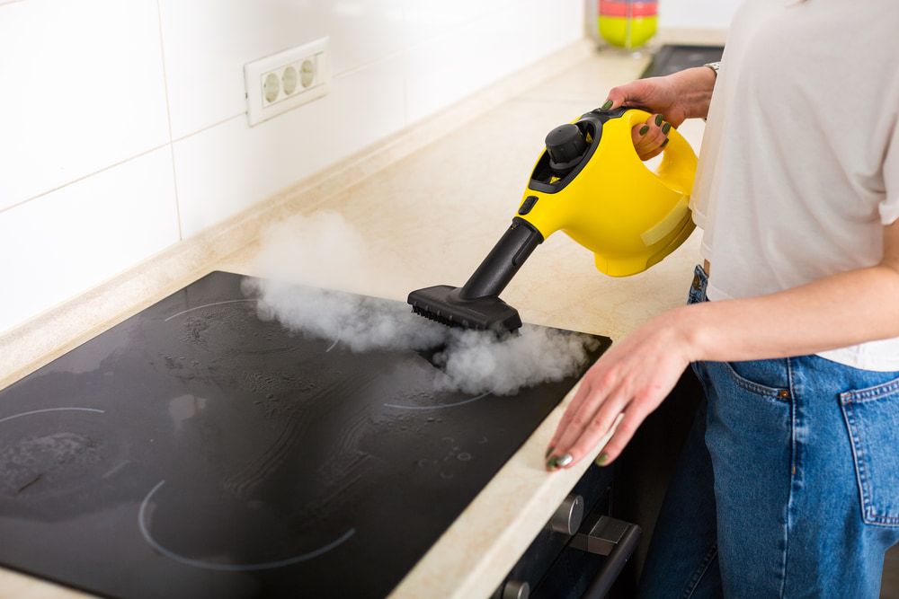 Woman is Cleaning a Stove Top With a Steam Cleaner — Happy Housekeepers in South Tamworth, NSW