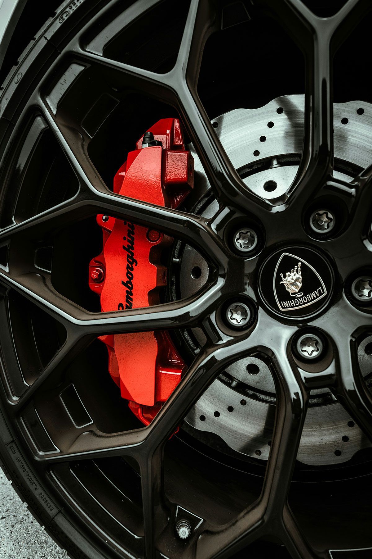 Close-up of a black Lamborghini wheel with red brake calipers and the Lamborghini logo.