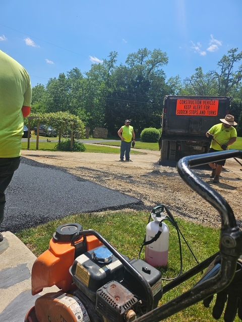 Workers with lawn equipment near a gravel lot and road sign on a sunny day