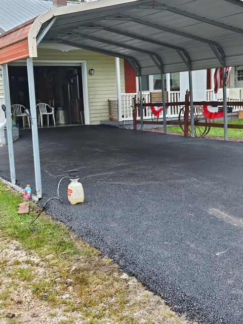 Covered carport with black gravel driveway beside a red house and white chairs inside.