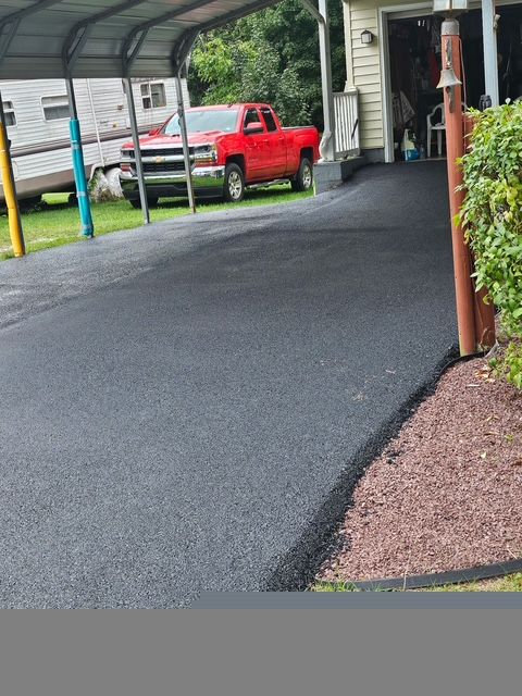Covered driveway with fresh black asphalt, a red pickup truck, and house porch at the side