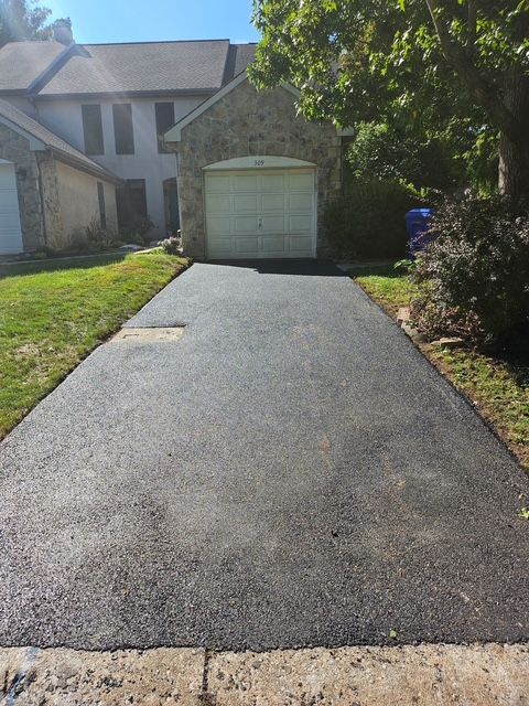Freshly paved black driveway leading to a white garage under a sunny suburban house