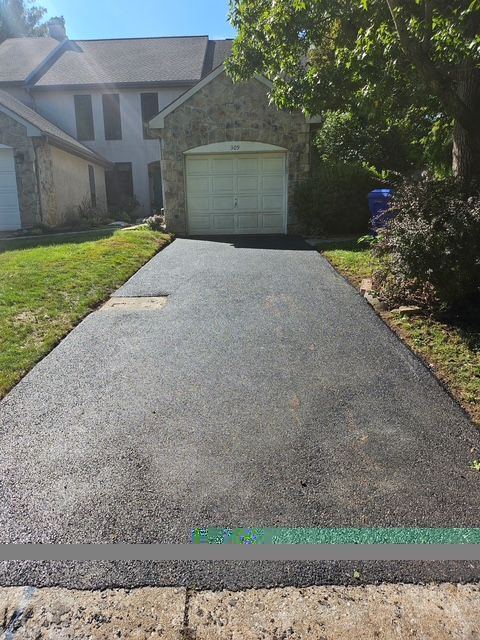 Freshly paved driveway leading to a stone house with a garage and green lawn