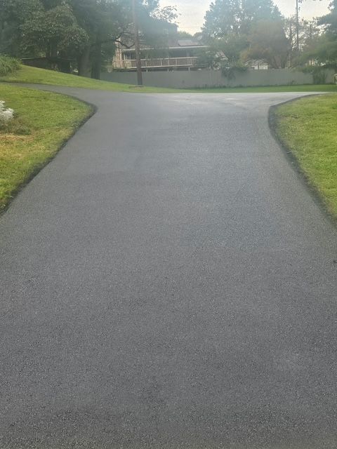 Curved paved driveway leading to a house, bordered by green grass and trees at dusk