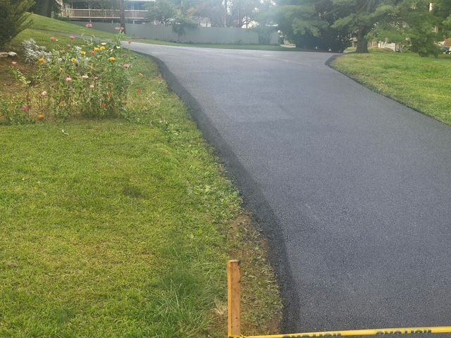 Curved paved driveway beside green lawn and flower bed in a quiet neighborhood