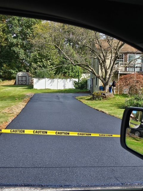 Freshly paved driveway with yellow caution tape and trees by a house