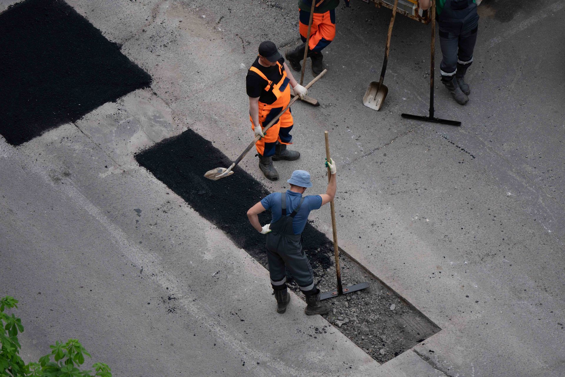 Construction workers in high-visibility gear paving a road with asphalt using shovels and a long-handled rake. Construction workers in high-visibility gear paving a road with asphalt using shovels and a long-handled rake.