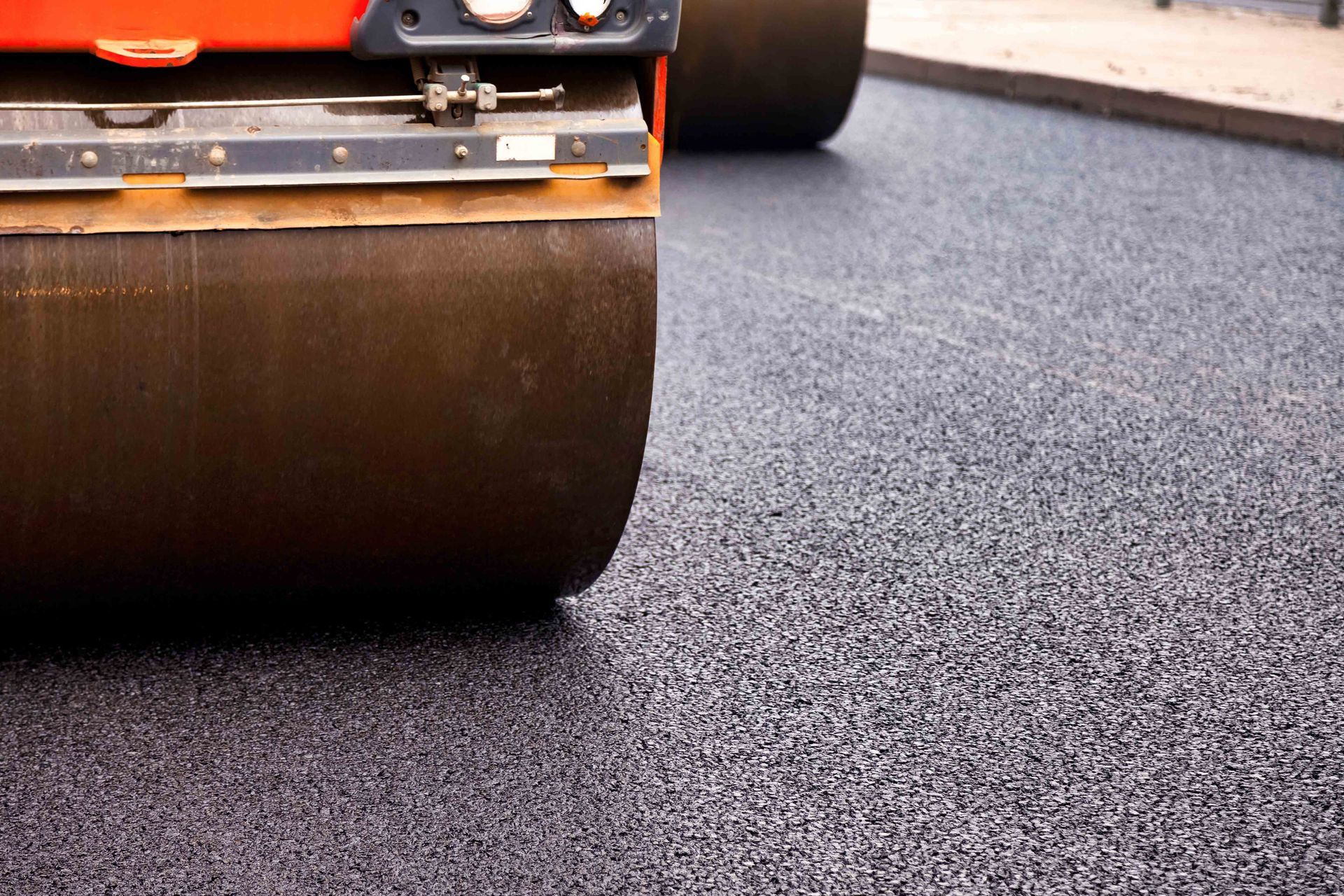 A heavy construction roller on a freshly laid, textured asphalt surface. A heavy construction roller on a freshly laid, textured asphalt surface.