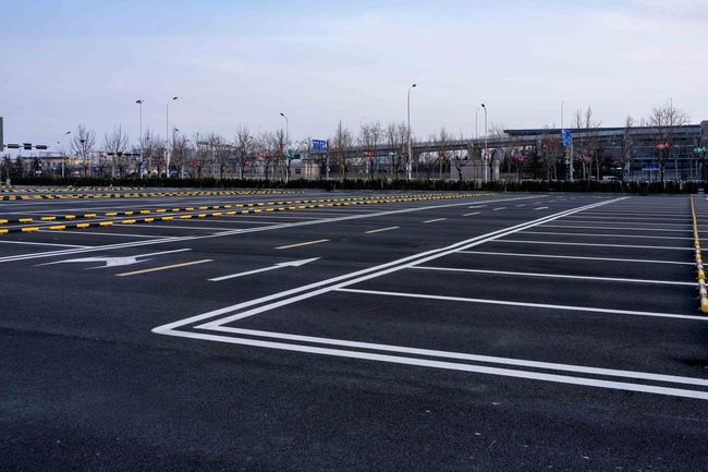 A nearly empty parking lot with clearly marked white stalls on asphalt under a pale sky.