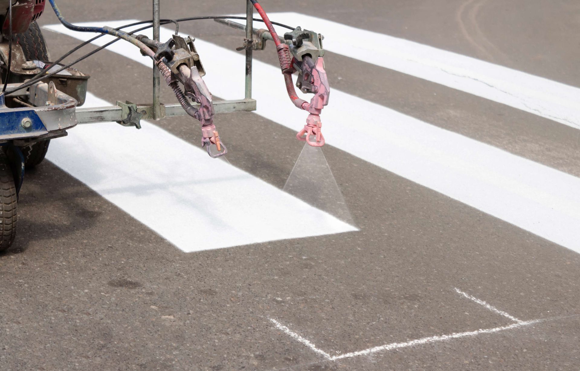 A mechanical sprayer paints white rectangular stripes on asphalt to create a pedestrian crosswalk. A mechanical sprayer paints white rectangular stripes on asphalt to create a pedestrian crosswalk.
