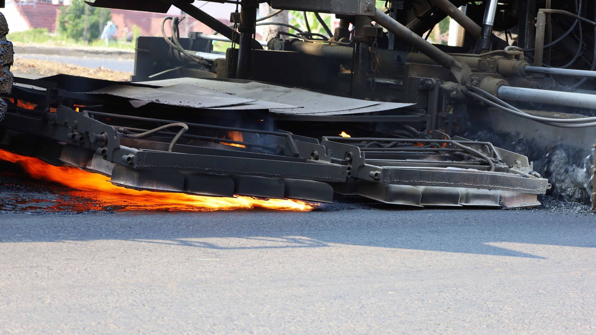 An asphalt heater machine uses an open flame to heat and soften the road surface during maintenance.