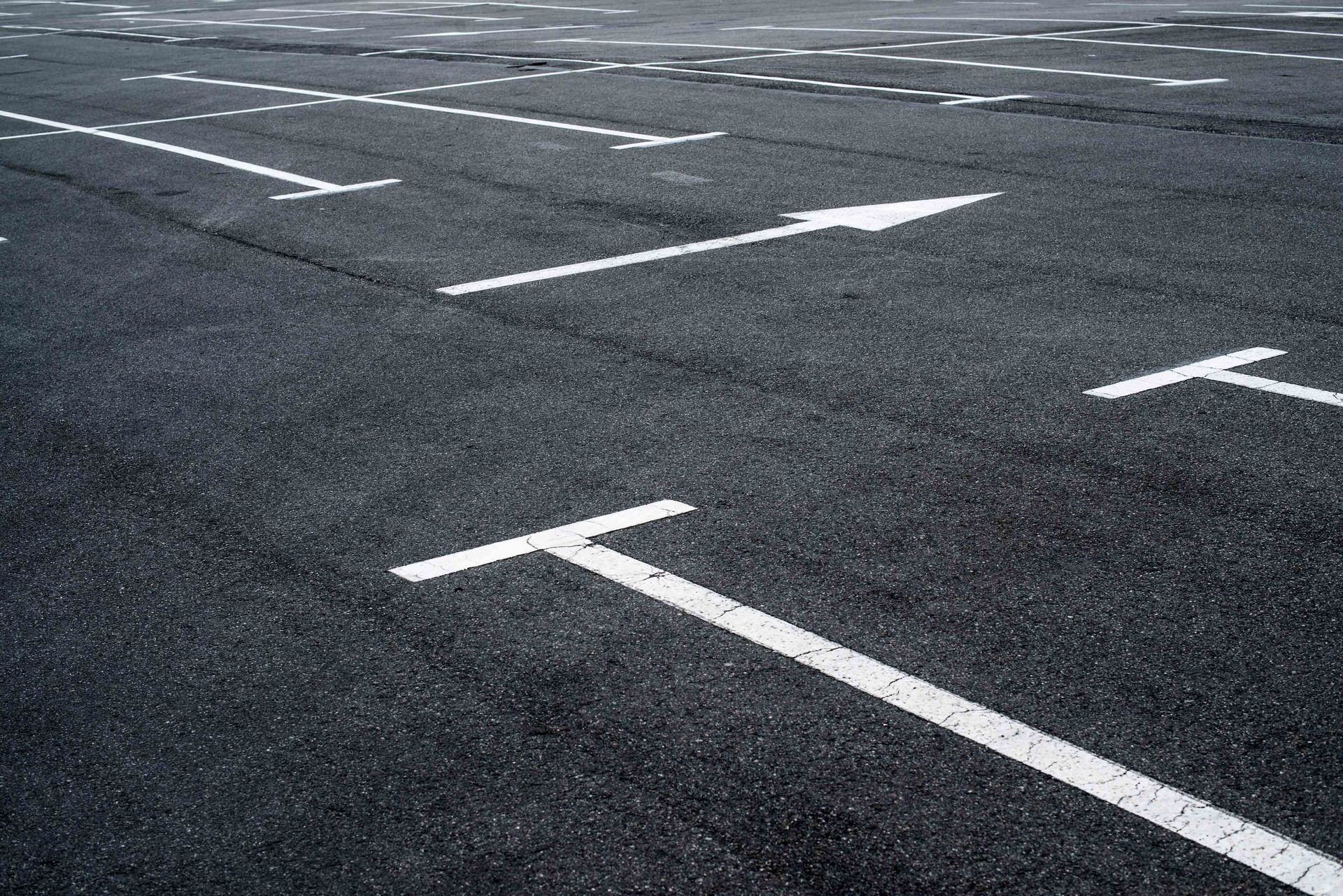 A series of white parking space lines painted on a dark asphalt surface, with an arrow indicating a traffic direction. A series of white parking space lines painted on a dark asphalt surface, with an arrow indicating a traffic direction.