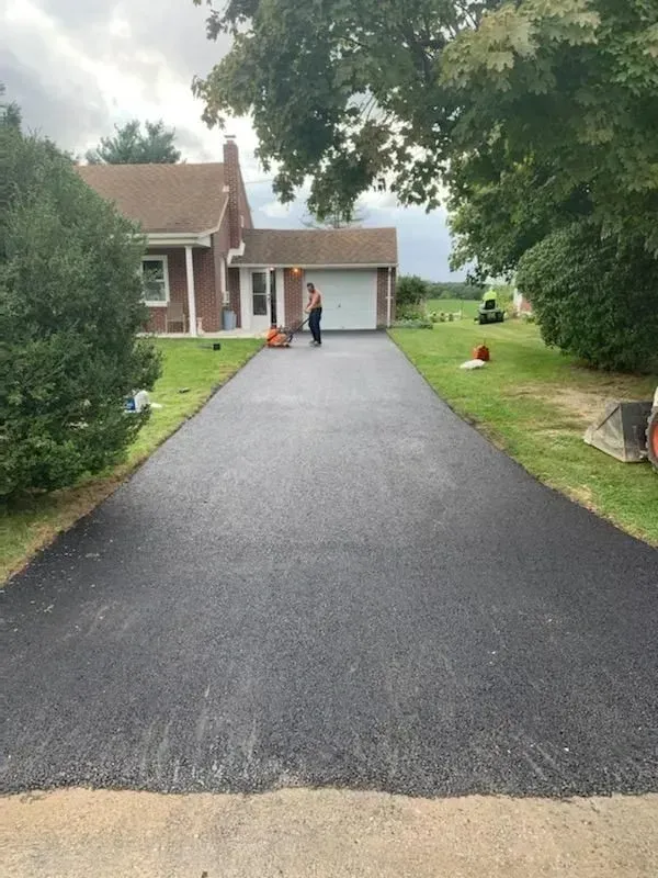 Freshly paved driveway leading to a house, with a person standing near the garage under cloudy skies