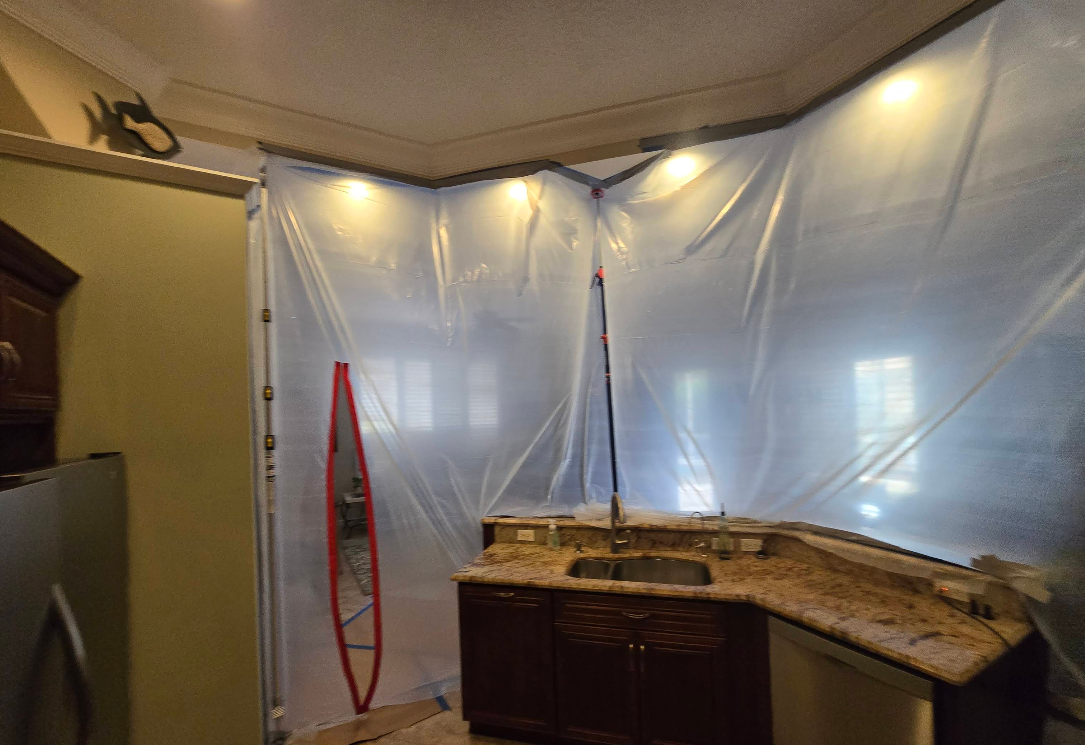 A kitchen counter and sink area sealed off with translucent plastic sheeting attached to the ceiling and walls.