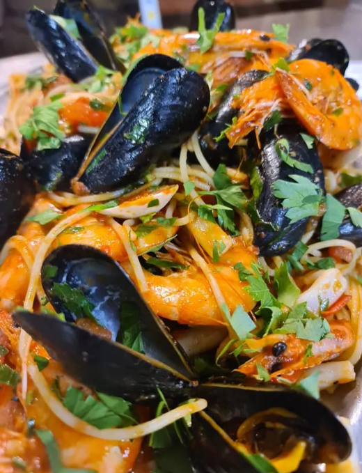 Pasta con cozze e gamberi, condita con erbe fresche e cipolle a fette.