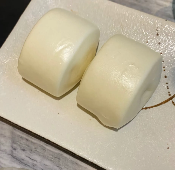 Due panini bianchi al vapore su un piatto bianco.