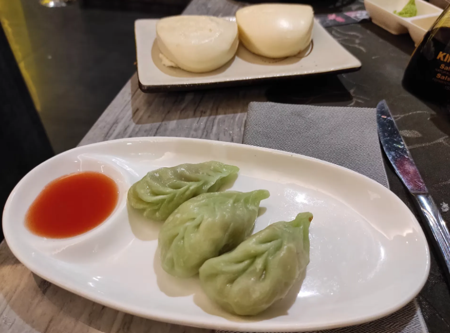 Tre ravioli verdi con salsa rossa su un piatto bianco a un tavolo di ristorante.