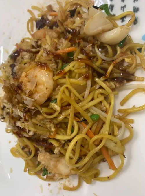 Piatto di spaghetti saltati in padella con gamberi, calamari e verdure, serviti su un piatto bianco.