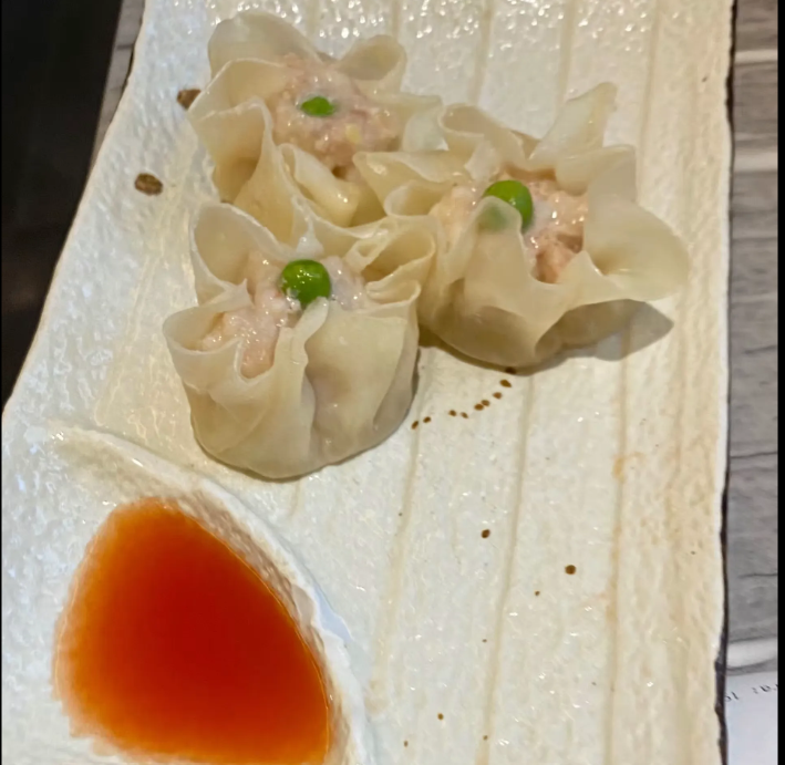 Ravioli al vapore serviti su un piatto bianco con salsa all'arancia e guarnizione di piselli.