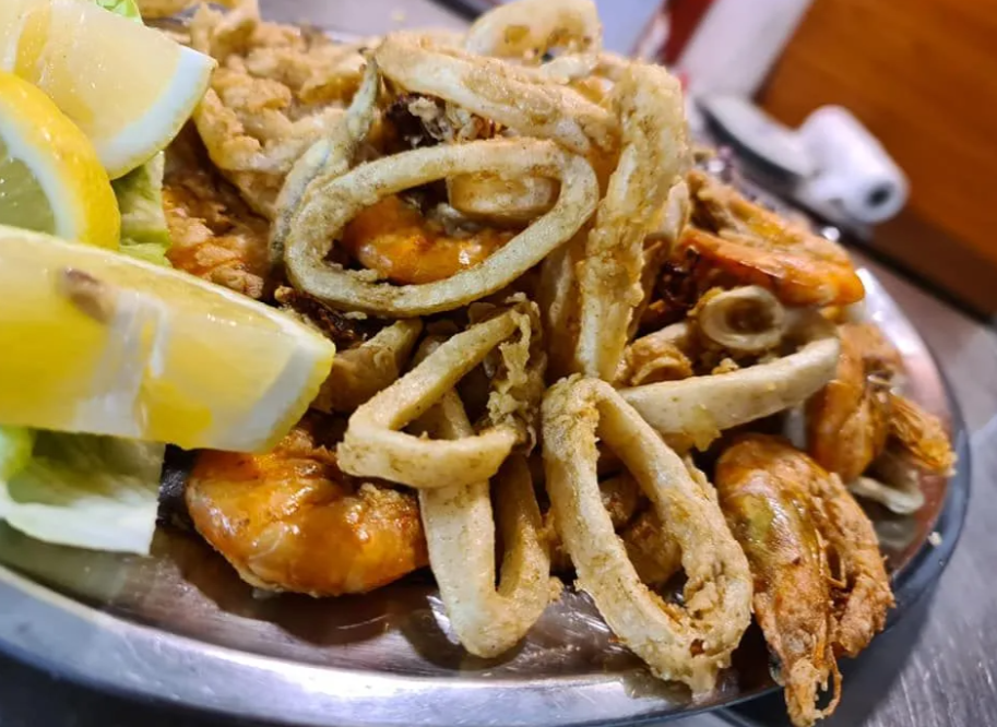 Piatto di frutti di mare fritti con calamari, gamberi e spicchi di limone su un piatto scuro