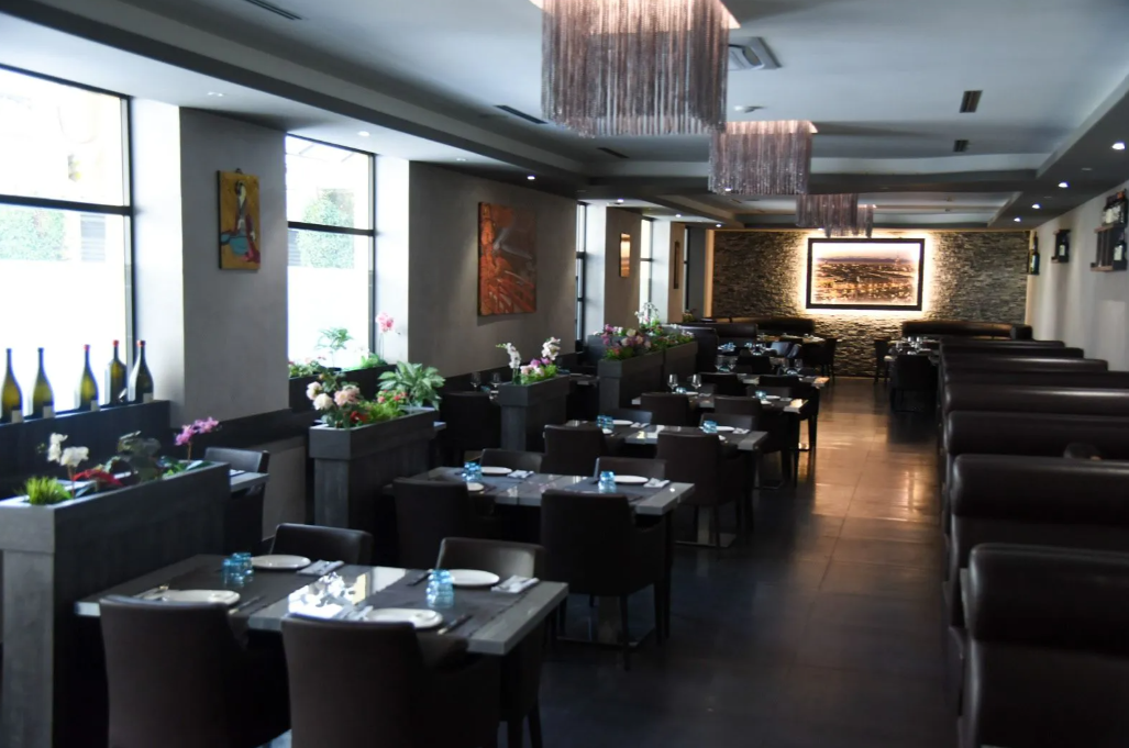 Sala da pranzo moderna del ristorante con tavoli neri, sedie bianche e ampie finestre che lasciano entrare la luce naturale.