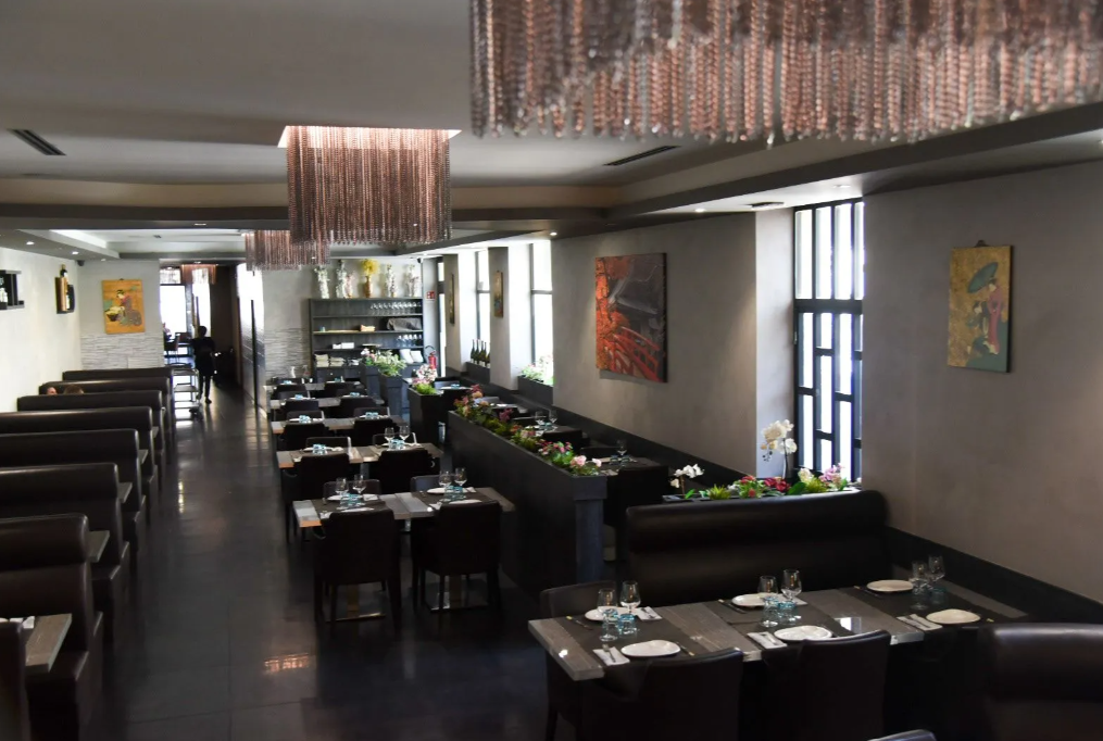 Sala da pranzo di un ristorante moderno con tavoli neri, posate bianche e decorazioni in rame sospese al soffitto.