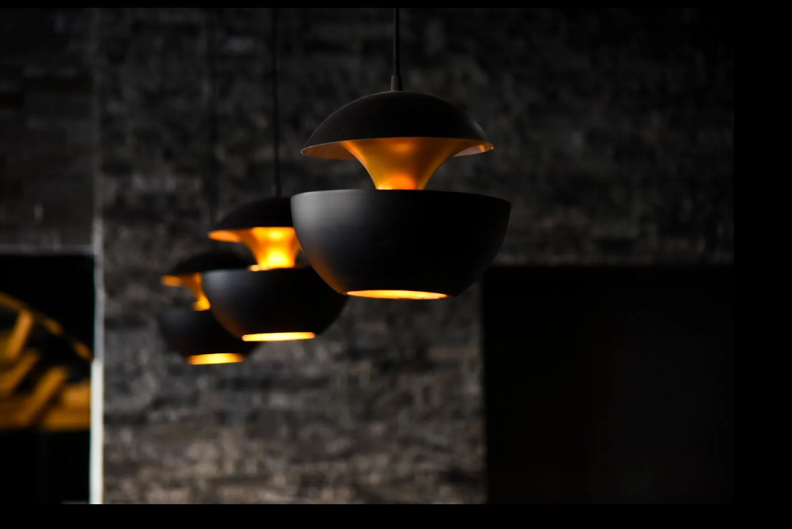 Tre lampade a sospensione nere con una calda luce arancione, appese a una parete scura e ruvida.