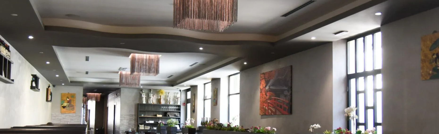 Hall moderna con lampadari, lucernari, opere d'arte alle pareti e ampie finestre che lasciano entrare la luce naturale.