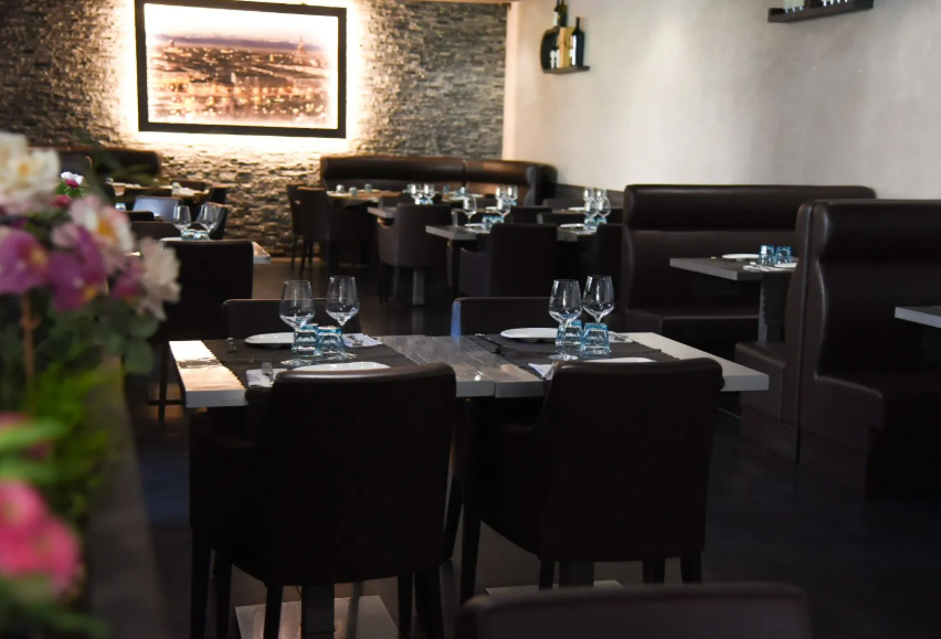 Sala da pranzo del ristorante in penombra con tavoli apparecchiati, divanetti scuri e un quadro incorniciato appeso alla parete.