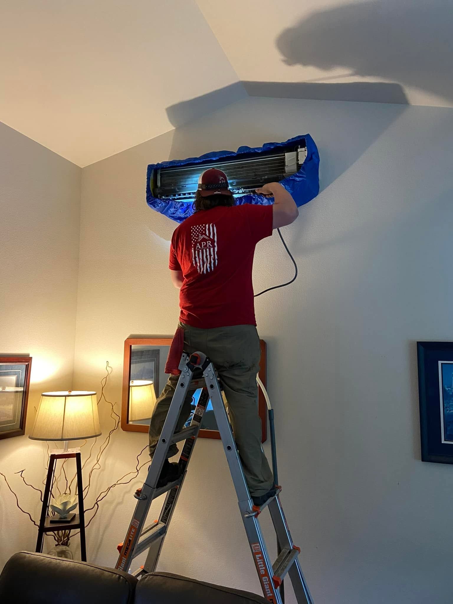 Person on a ladder installing a wall-mounted TV in a living room.