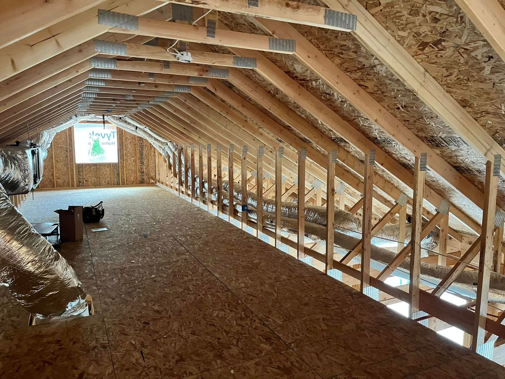 Attic interior with exposed wooden rafters, insulation, and unfinished floor decking