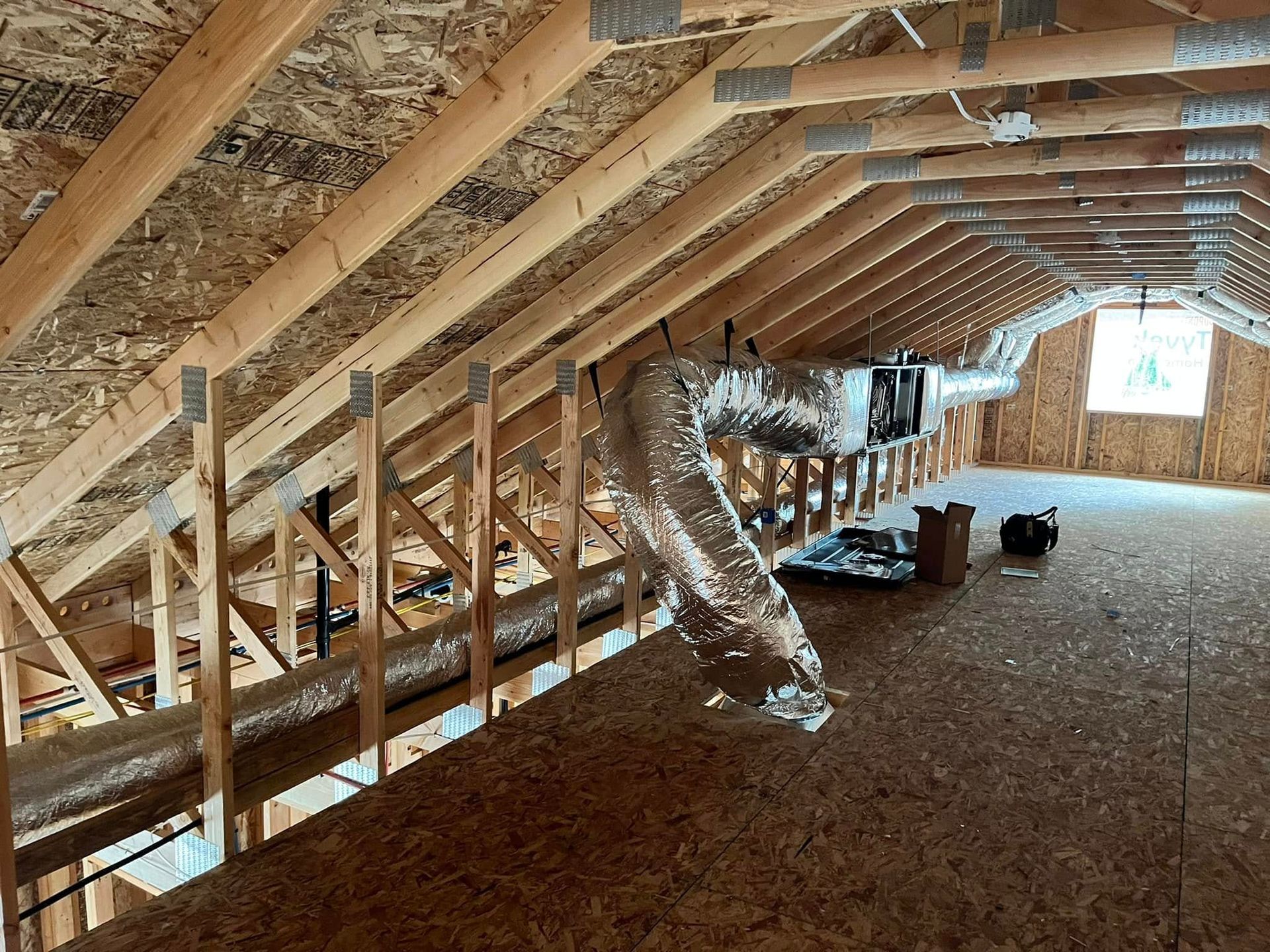 Attic interior with exposed rafters, ductwork, insulation, and unfinished flooring under construction