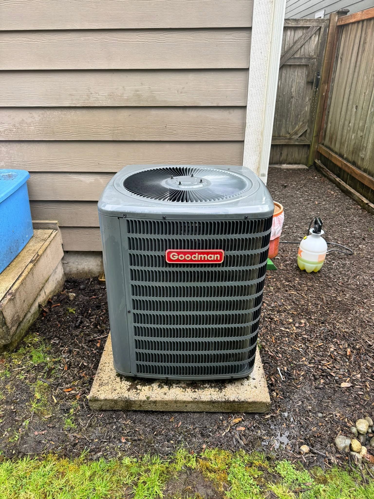 Outdoor air conditioner unit beside a house, with a spray bottle nearby on a gravel bed.