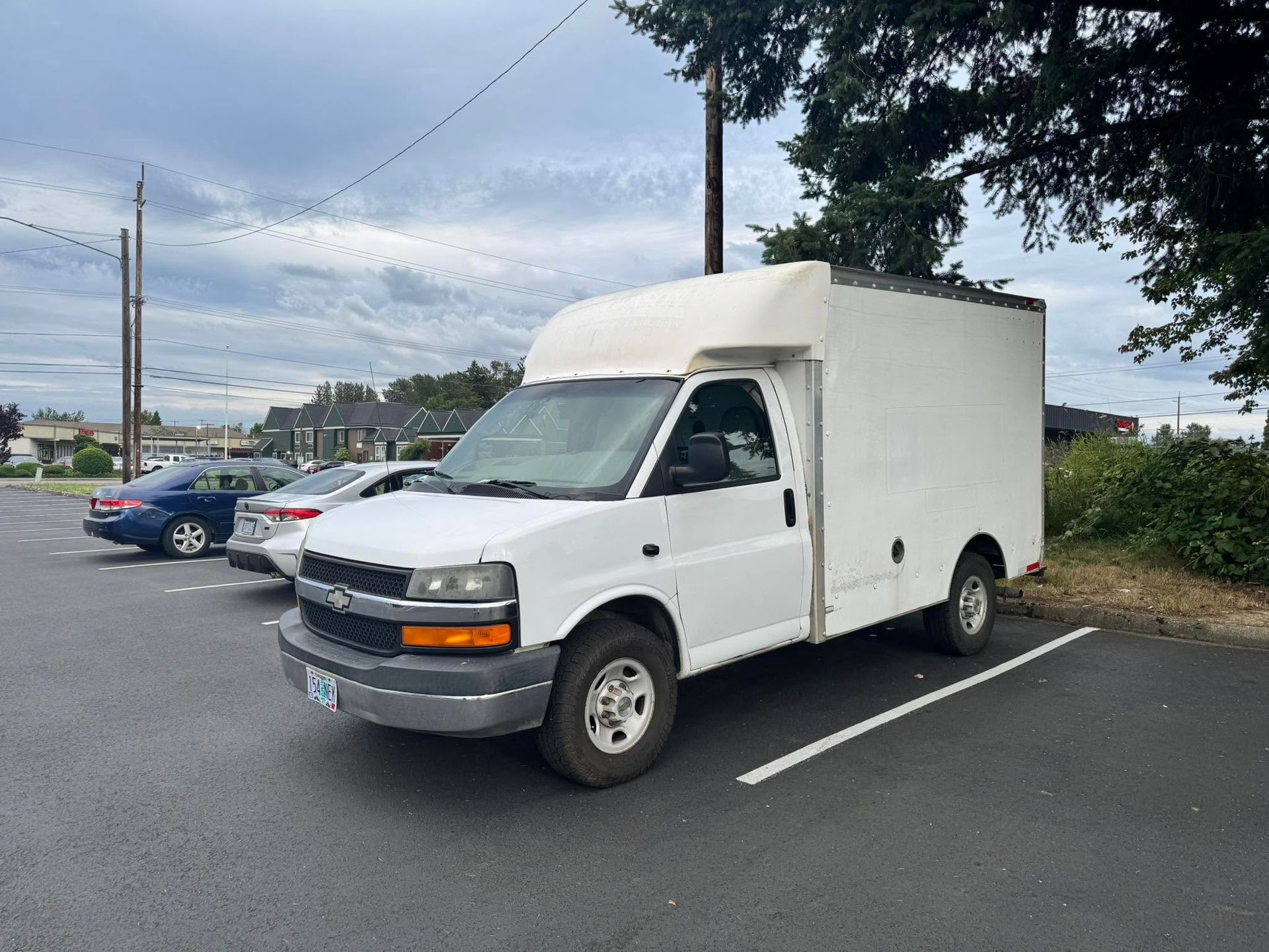 White box truck parked in a lot under a cloudy sky, seen from the front-left.