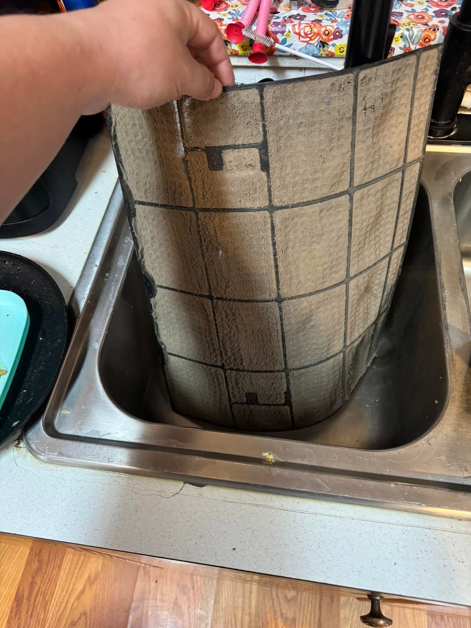 Hand placing a rolled mat into a kitchen sink beside colorful items on the counter